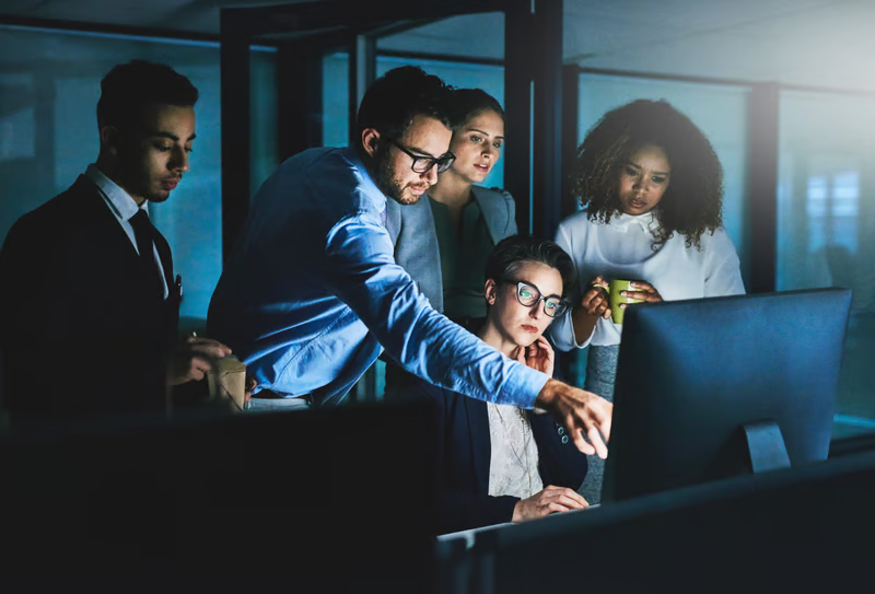 A workforce team collaborating at computer workstations in a dark office